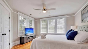 A bedroom with a bed, a television, a ceiling fan, and large windows with blinds. - Spacious 3BR Home, Walk to King St! (Charleston)
