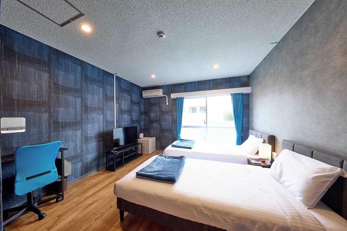 Et moderne hotelværelse med to senge, et skrivebord, en stol og et fjernsyn.