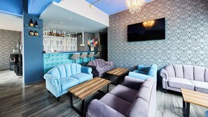 A modern lounge area with sofas, tables, a bar, and a TV.