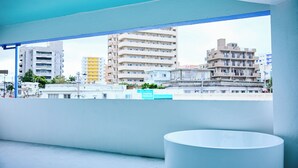 A balcony with a view of urban buildings, a white cylindrical object, and a blue ceiling.