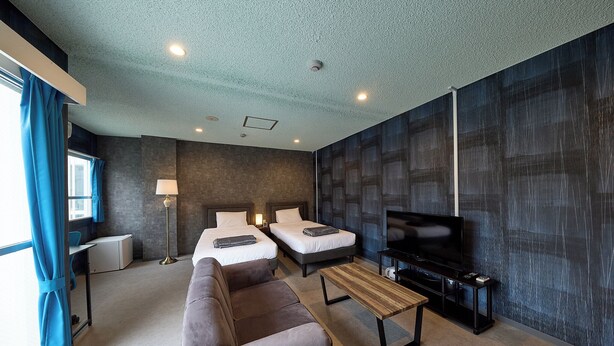 A modern hotel room with two beds, a sofa, a TV, and a desk.