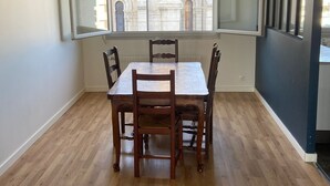 A dining area with a wooden table and chairs, a hanging light fixture, and a view of a building through a window. - Family housing - Lyon 6e/Villeurbanne - Charpennes (Villeurbanne)