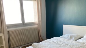 A bedroom with a white bed, a blue wall, and a window with curtains. - Family housing - Lyon 6e/Villeurbanne - Charpennes (Villeurbanne)