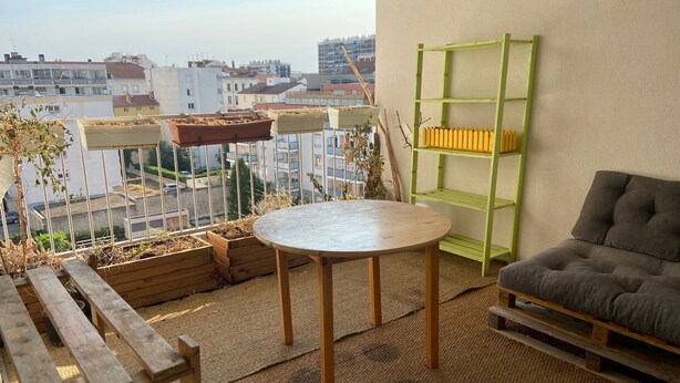 A balcony with a round table, wooden benches, a green shelf, and a gray sofa. - Family housing - Lyon 6e/Villeurbanne - Charpennes (Villeurbanne)
