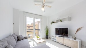 Una sala de estar moderna con un sofá gris, una mesa de centro, un televisor sobre un mueble blanco y un ventilador de techo.