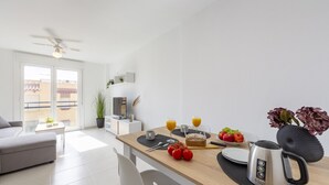 Una habitación moderna y bien iluminada con una mesa de comedor lista para el desayuno, un sofá y un ventilador de techo.