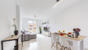 Una sala de estar y comedor moderna y minimalista, con un sofá, una mesa de comedor con sillas, un televisor y un ventilador de techo.
