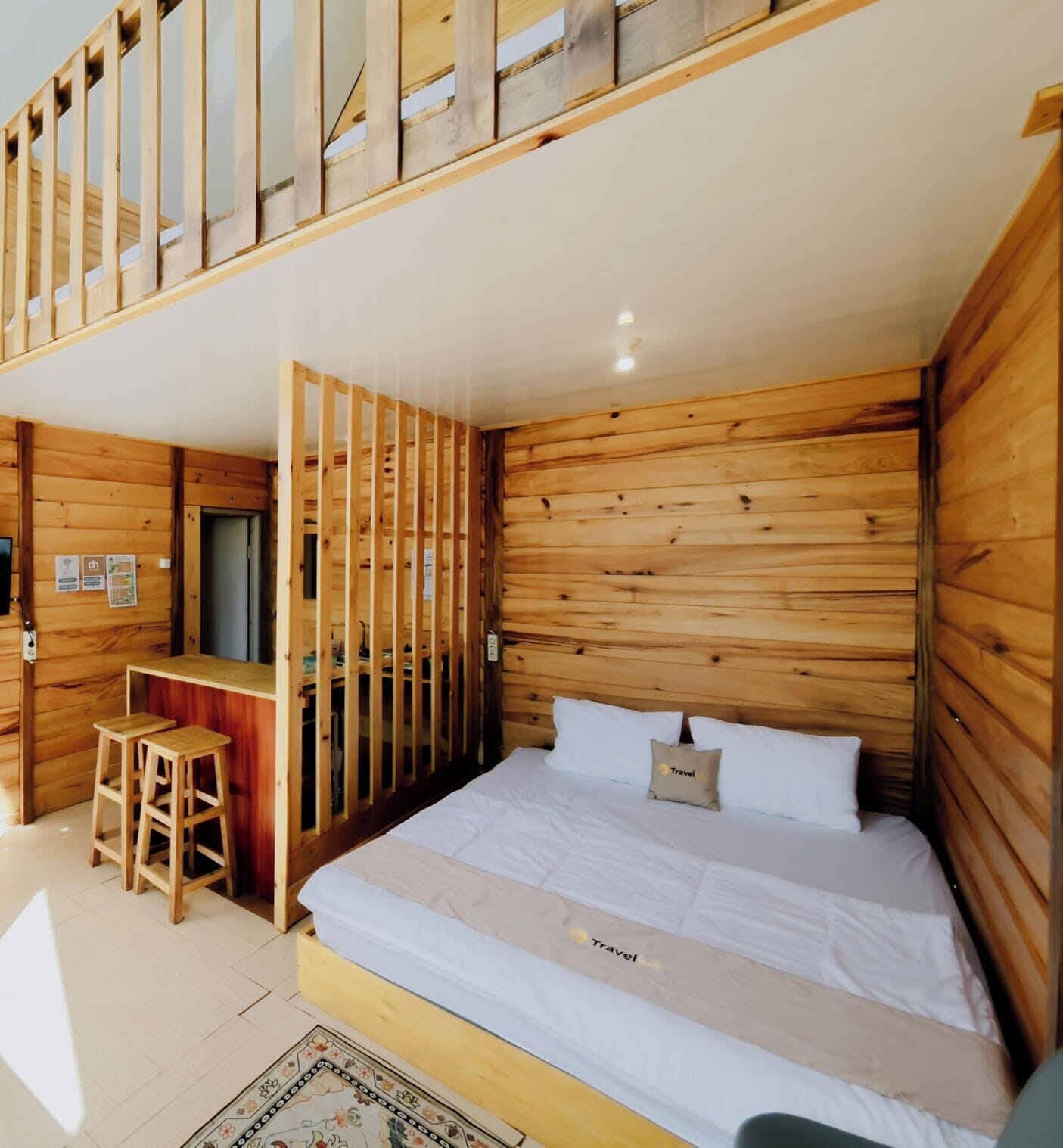 A wooden cabin-style room with a bed, a small desk, and a stool.
