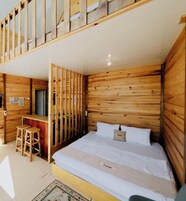 Um quarto estilo cabana de madeira com uma cama, uma escrivaninha pequena e um banquinho.