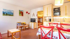 A compact room with a bunk bed, a television, a small table, and a kitchen area with a microwave.