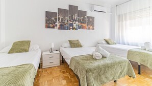 A hotel room with three beds, a nightstand, a wall-mounted air conditioner, and a large window with sheer curtains. - Your Large Family Apartment in Zaragoza (Zaragoza)