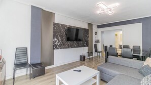 A modern living room with a flat-screen TV mounted on a marble wall, grey sofas, a white coffee table, and a dining area in the background. - Your Large Family Apartment in Zaragoza (Zaragoza)