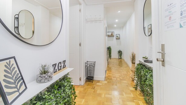 A hallway with white walls, wooden flooring, and mirrors on both sides. There are plants on the floor and a shelf with a sign. - Your Large Family Apartment in Zaragoza (Zaragoza)