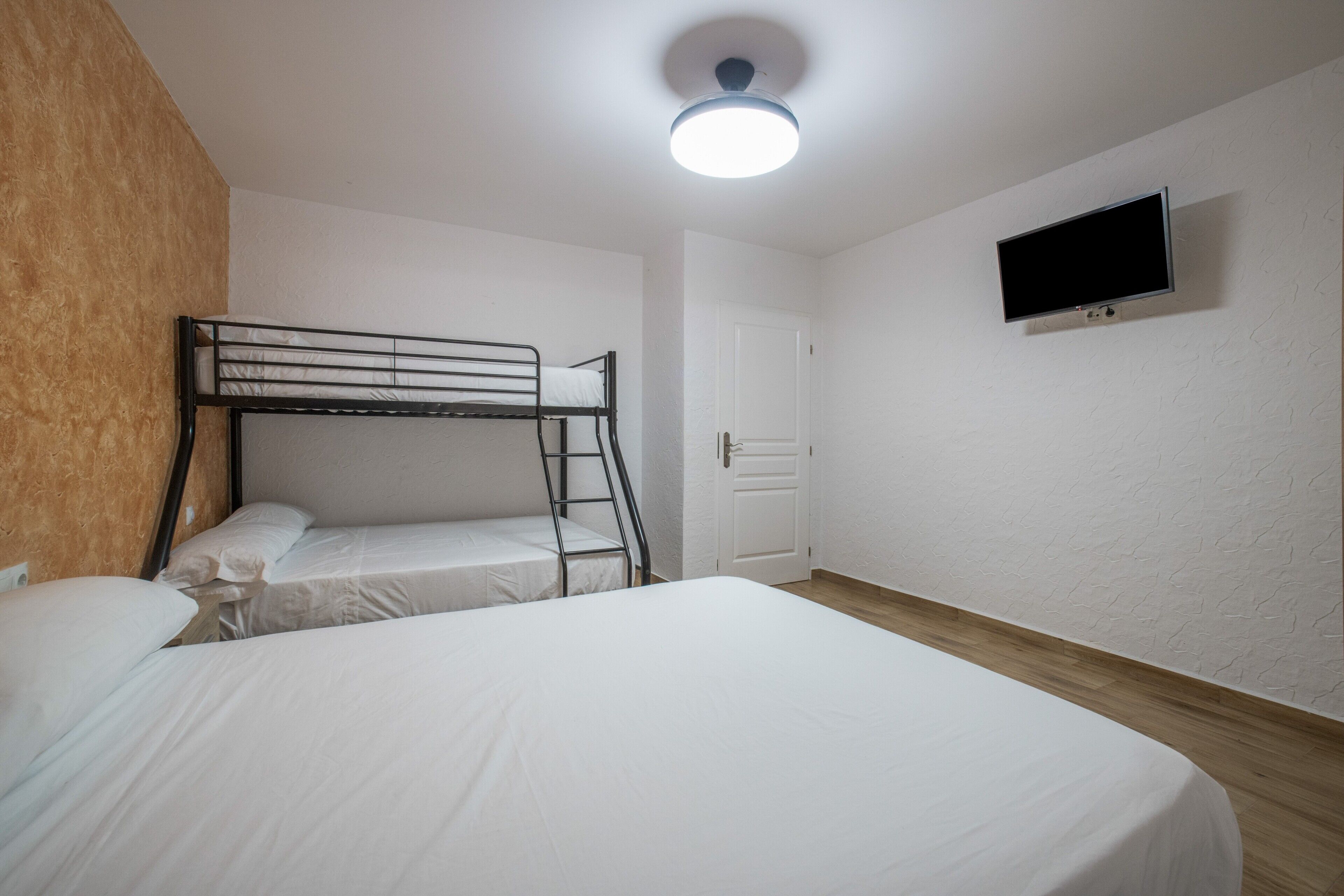 Een kamer met stapelbedden, een aan de muur bevestigde televisie en een deur.