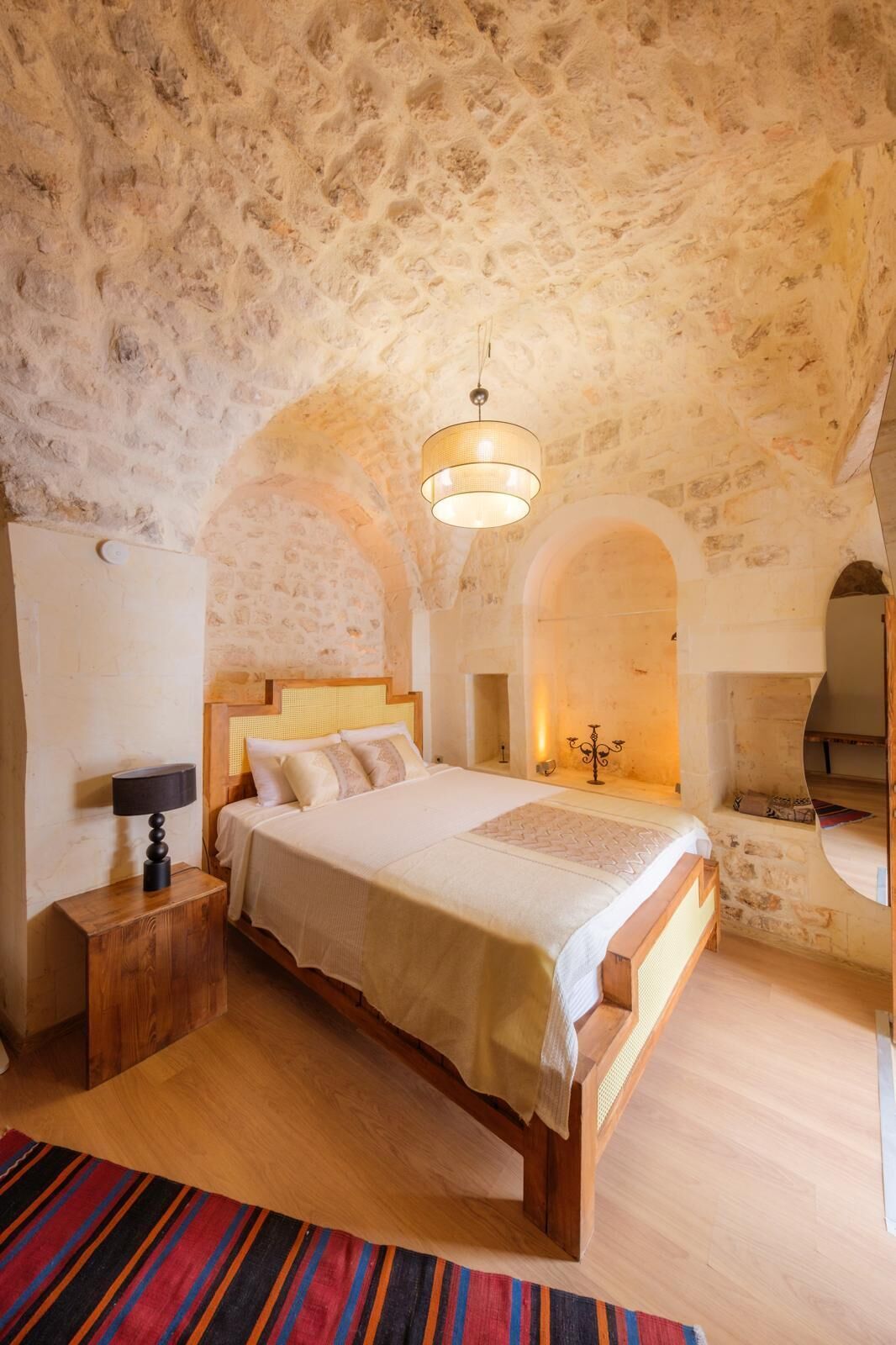 A bedroom with a stone ceiling, a bed, a nightstand, a lamp, and a candelabra.