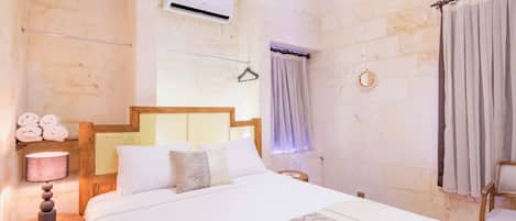 A hotel room with a bed, bedside table, lamp, air conditioning unit, and a hanging light fixture.