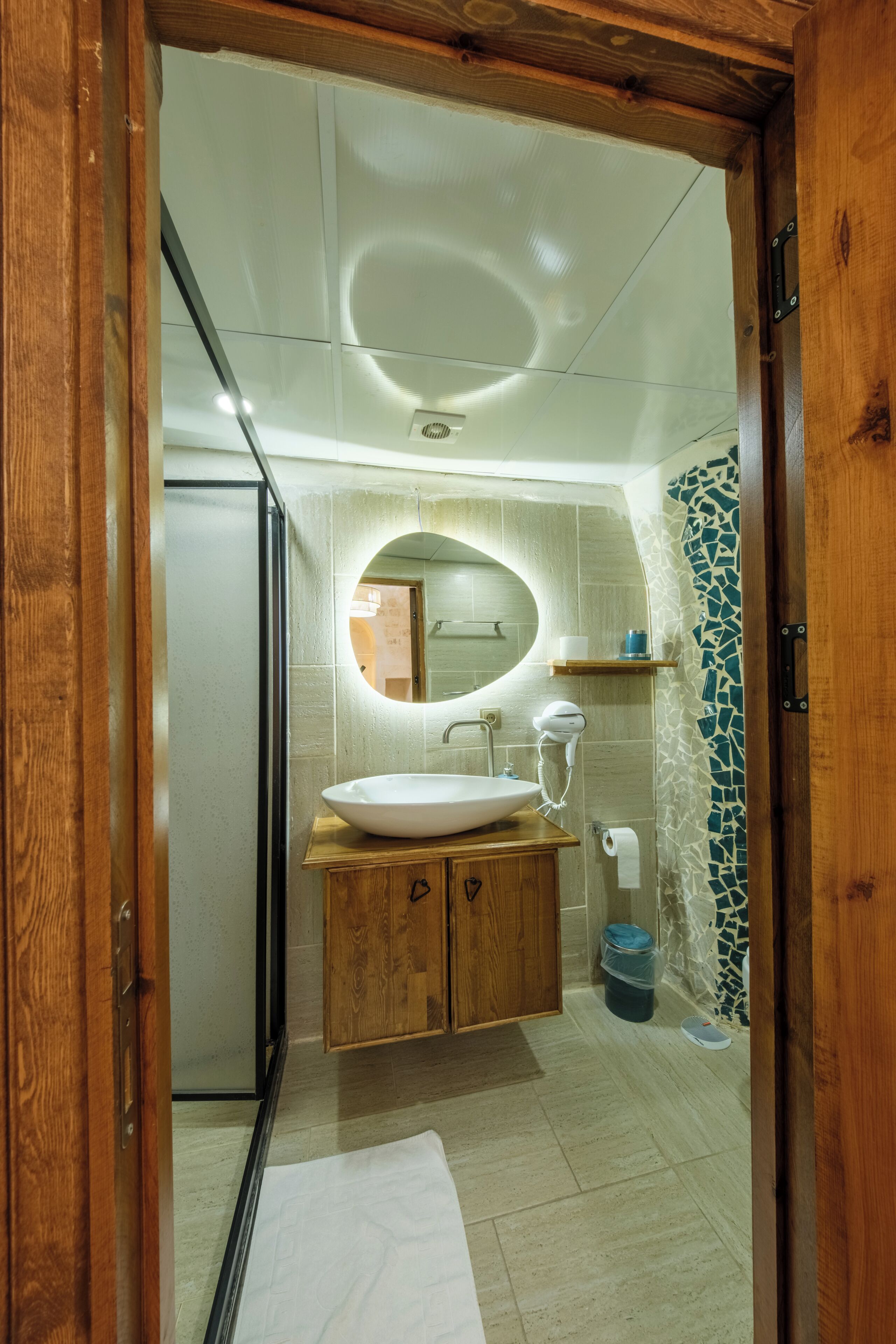 A bathroom with a wooden vanity, a round mirror, a white sink, and a shower area.