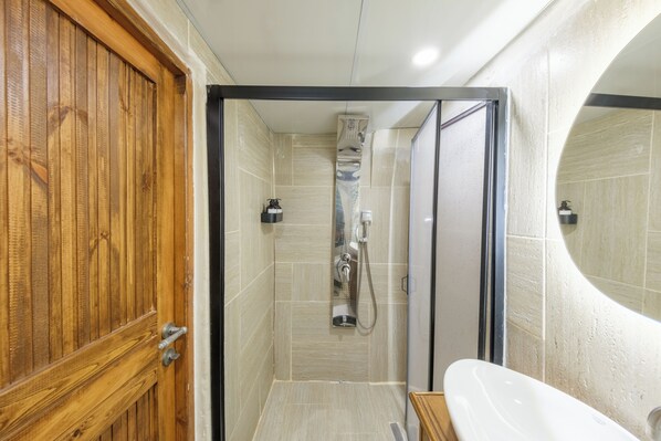 A bathroom with a wooden door, a shower with a handheld showerhead, and a white sink.