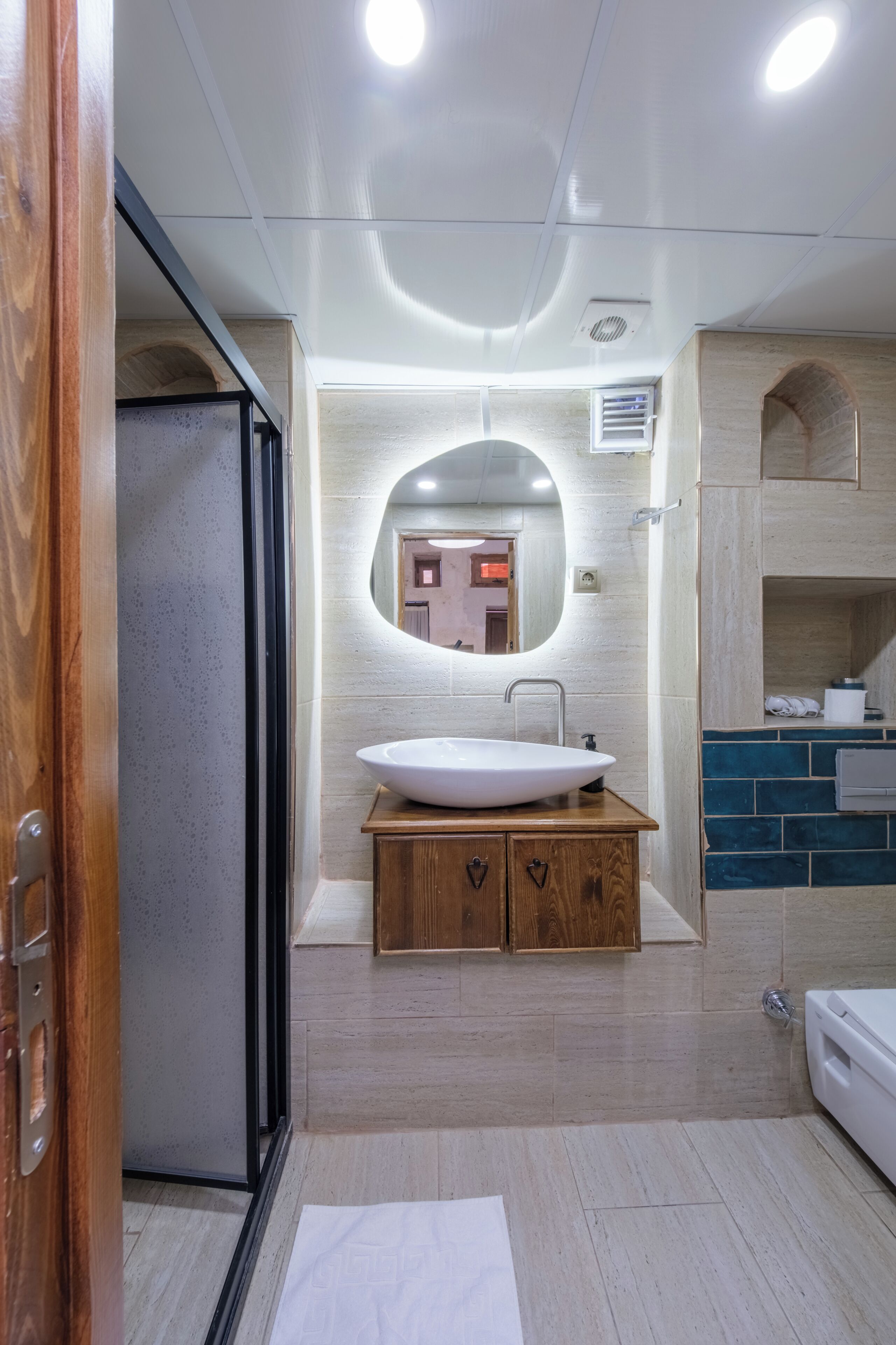 Une salle de bain avec un meuble-lavabo en bois, un lavabo blanc et un miroir rond.
