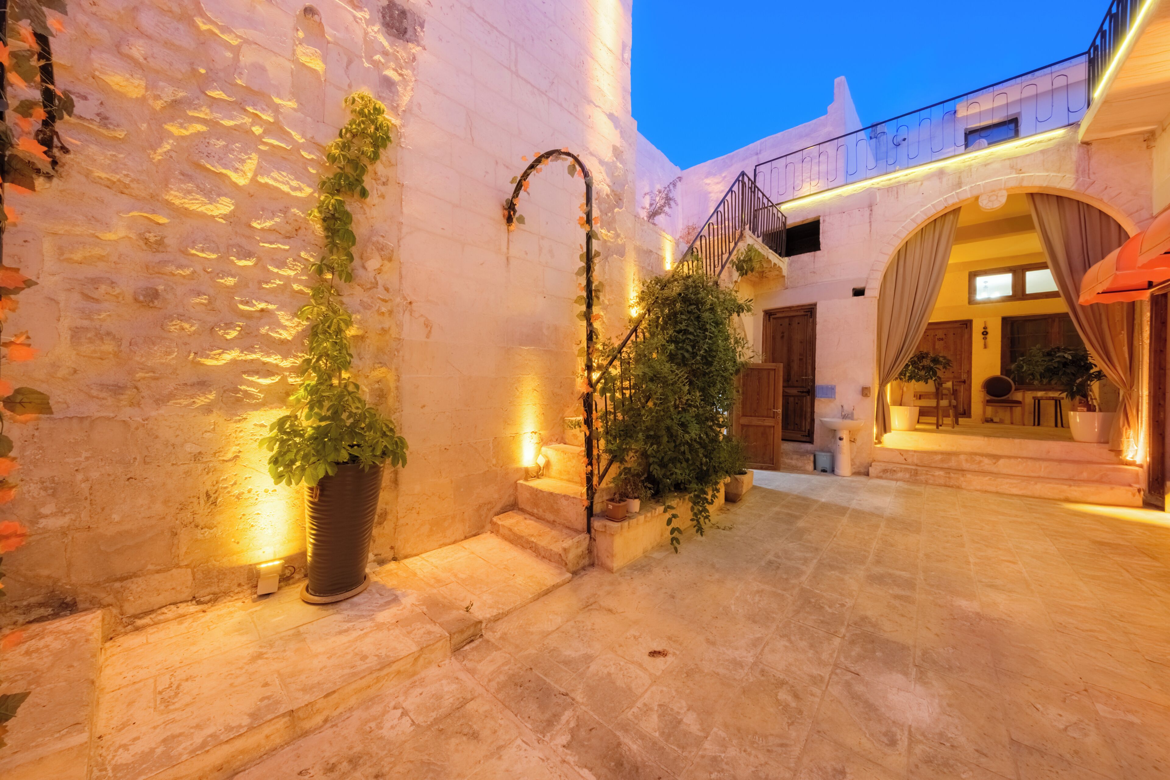 A stone courtyard with a staircase, potted plants, and a building entrance.