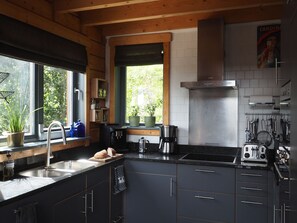 Een moderne keuken met roestvrijstalen apparatuur, houten balken en een raam met uitzicht op groen.