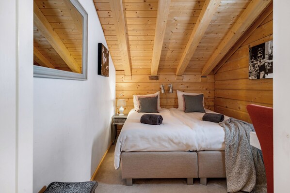 A cozy bedroom with a wooden ceiling, a large bed with pillows, a bedside table with a lamp, and a window. - Renewed! 4-minute walk to skilift & skilockers! 10 min. walk to spa! No bunkbeds (Les Collons 1800m)