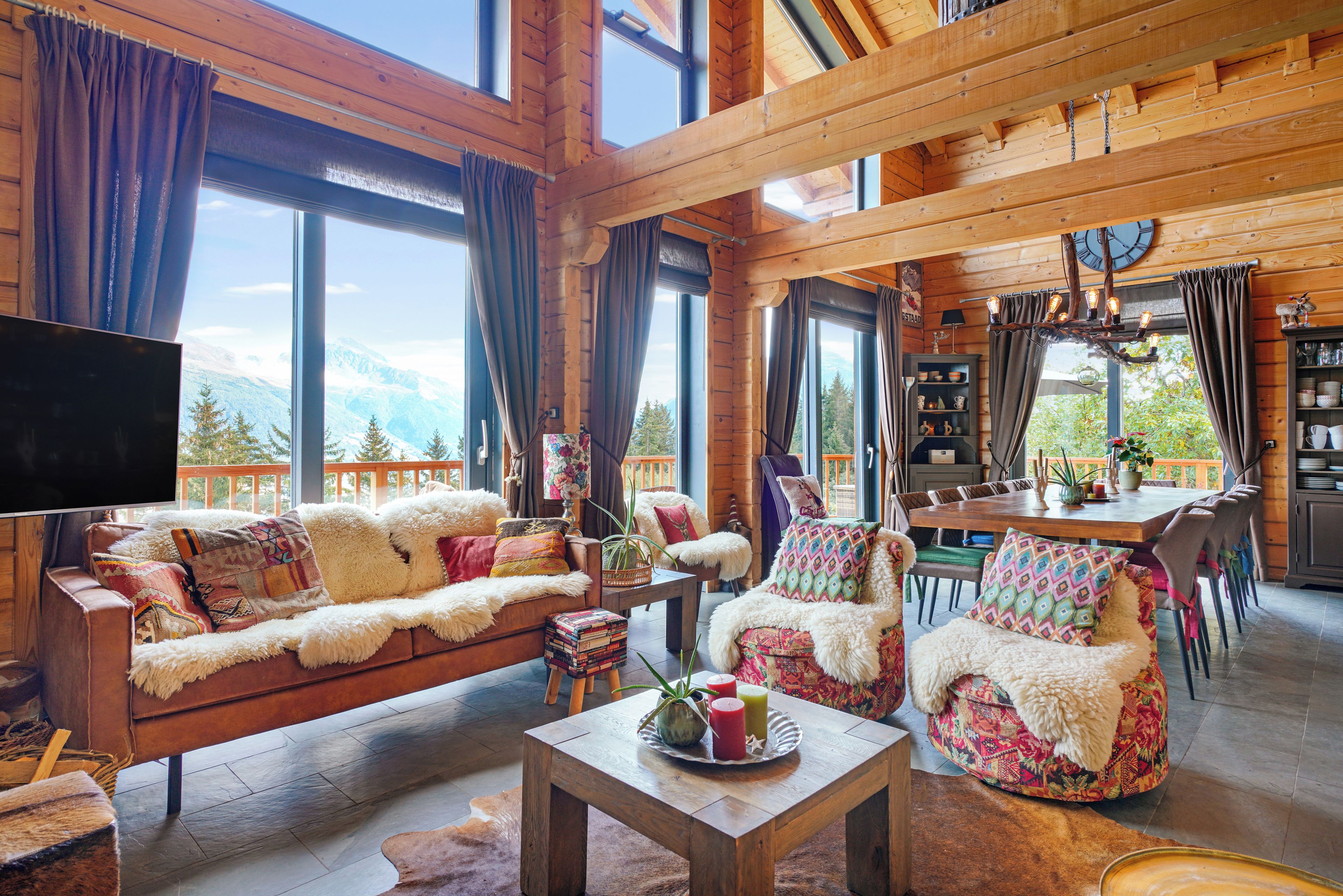 Un intérieur de chalet chaleureux avec un canapé, des fauteuils, une table à manger et un téléviseur.