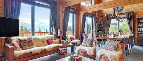 A cozy cabin interior with a sofa, chairs, a dining table, and a TV.