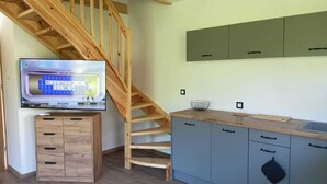 A kitchen with wooden cabinets, a wooden staircase, and a television displaying a game. - New, Comfortable Holiday Home by the sea (gmina Karnice)