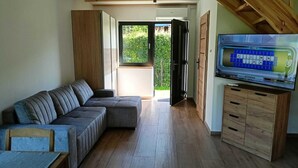 A modern living room with a sectional sofa, wooden flooring, a TV on a wooden cabinet, and a sliding glass door leading to a balcony. - New, Comfortable Holiday Home by the sea (gmina Karnice)