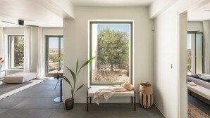 A modern interior with a large window, a bench, a potted plant, and a woven basket. - Ampelas 4BR Villa, Private Pool, To Ktima Paros (Paros)