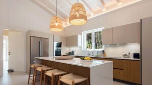 Una cucina moderna con isola centrale, sgabelli da bar, elettrodomestici in acciaio inossidabile e illuminazione a sospensione.