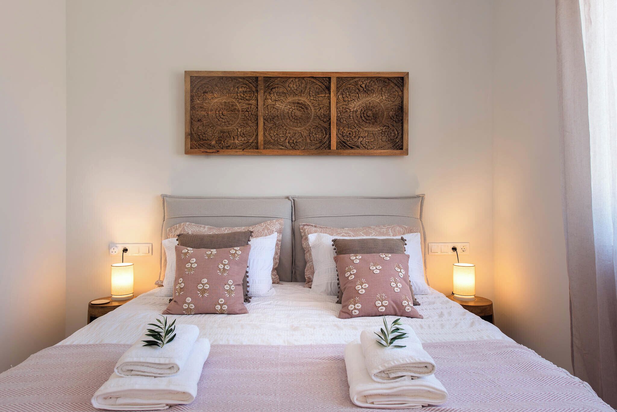 Una cama bien hecha con dos almohadas, una lámpara de noche y una obra de arte en la pared.
