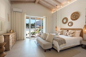 A bedroom with a large bed, a wooden bench, a bedside table, and a view of the outside.
