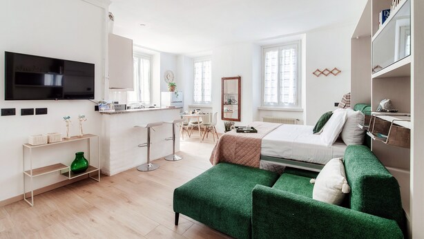A modern, well-lit room with a bed, green upholstered furniture, a TV, and a kitchenette. - Dinghy Studio (Como)