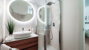 A modern bathroom with a glass-enclosed shower, a large oval mirror, and a wooden vanity. - Dinghy Studio (Como)