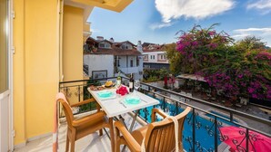 Un balcón con mesa dispuesta para dos, sillas, una piscina y vistas a edificios y buganvillas.