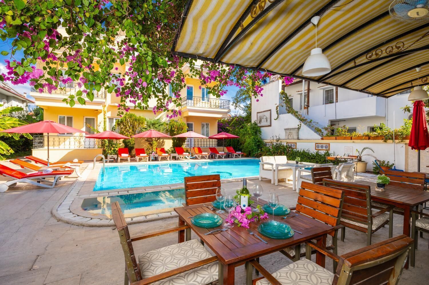 Un área junto a la piscina con mesa lista para comer, sillas de descanso y sombrillas.