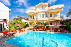 Un hotel con piscina, sombrillas rojas y sillas de descanso.