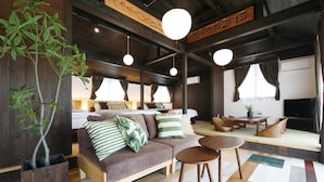 A cozy living room with a sofa, two round tables, and a large plant. - Ryukyu Kominka Yamakawa House (Motobu)