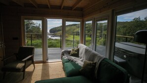 Une pièce confortable avec un canapé vert, un fauteuil et une grande porte-fenêtre coulissante donnant sur un balcon offrant une vue magnifique.