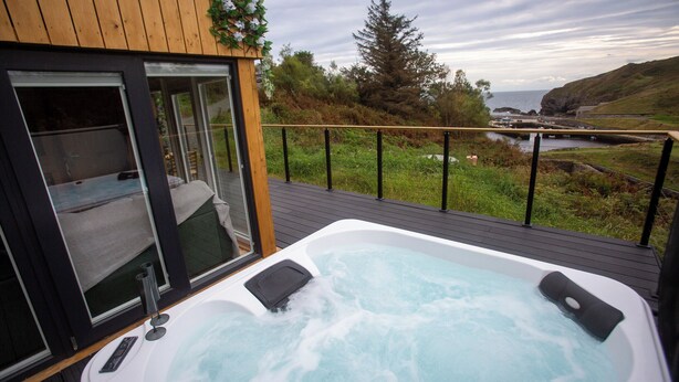 Un bain à remous sur une terrasse en bois, avec vue sur la mer et les collines.