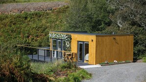 Une petite cabane en bois avec une porte et des fenêtres en verre, entourée de verdure.