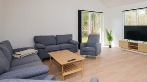 A modern living room with a grey sofa, a smaller grey armchair, a wooden coffee table, and a TV on a wooden stand. - 5 Star Holiday Home in Ansager (Ansager)