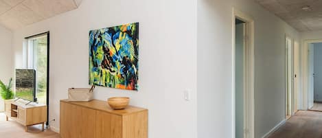 A modern interior with a wooden cabinet, a colorful abstract painting, and a view through a window.