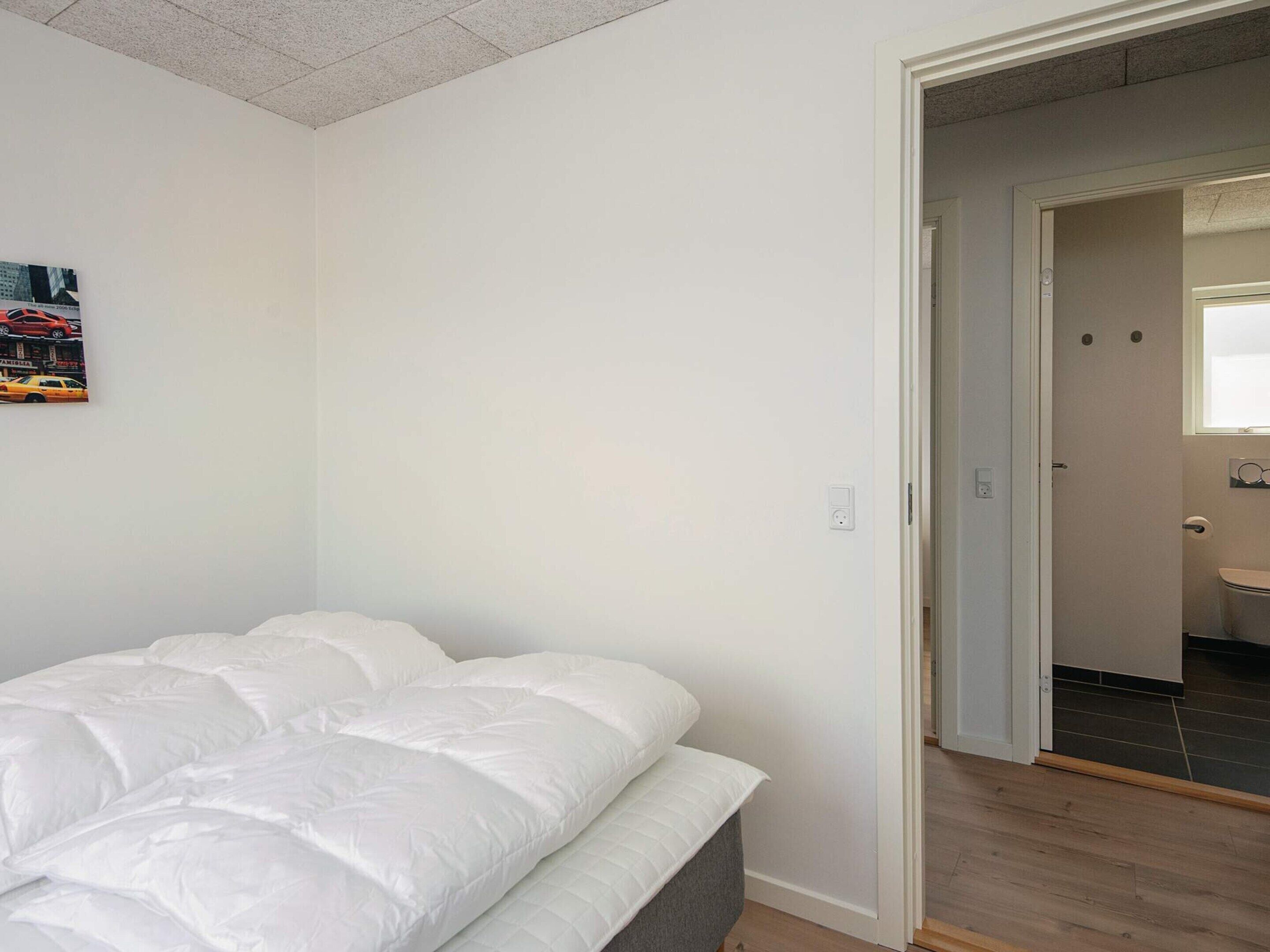 Une chambre à coucher avec un lit, une porte donnant sur une salle de bain et un interrupteur fixé au mur.