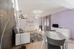 A modern living room with a dining table, sofa, and a TV on a white cabinet.