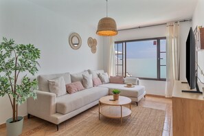 A modern living room with a sofa, a round coffee table, a potted plant, and a television. - Vacation Home 'Timanfaya' with Sea View, Private Pool and Wi-Fi (Tías)
