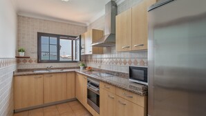 A kitchen with wooden cabinets, a stainless steel refrigerator, a built-in oven, and a window with a view. - Vacation Home 'Timanfaya' with Sea View, Private Pool and Wi-Fi (Tías)