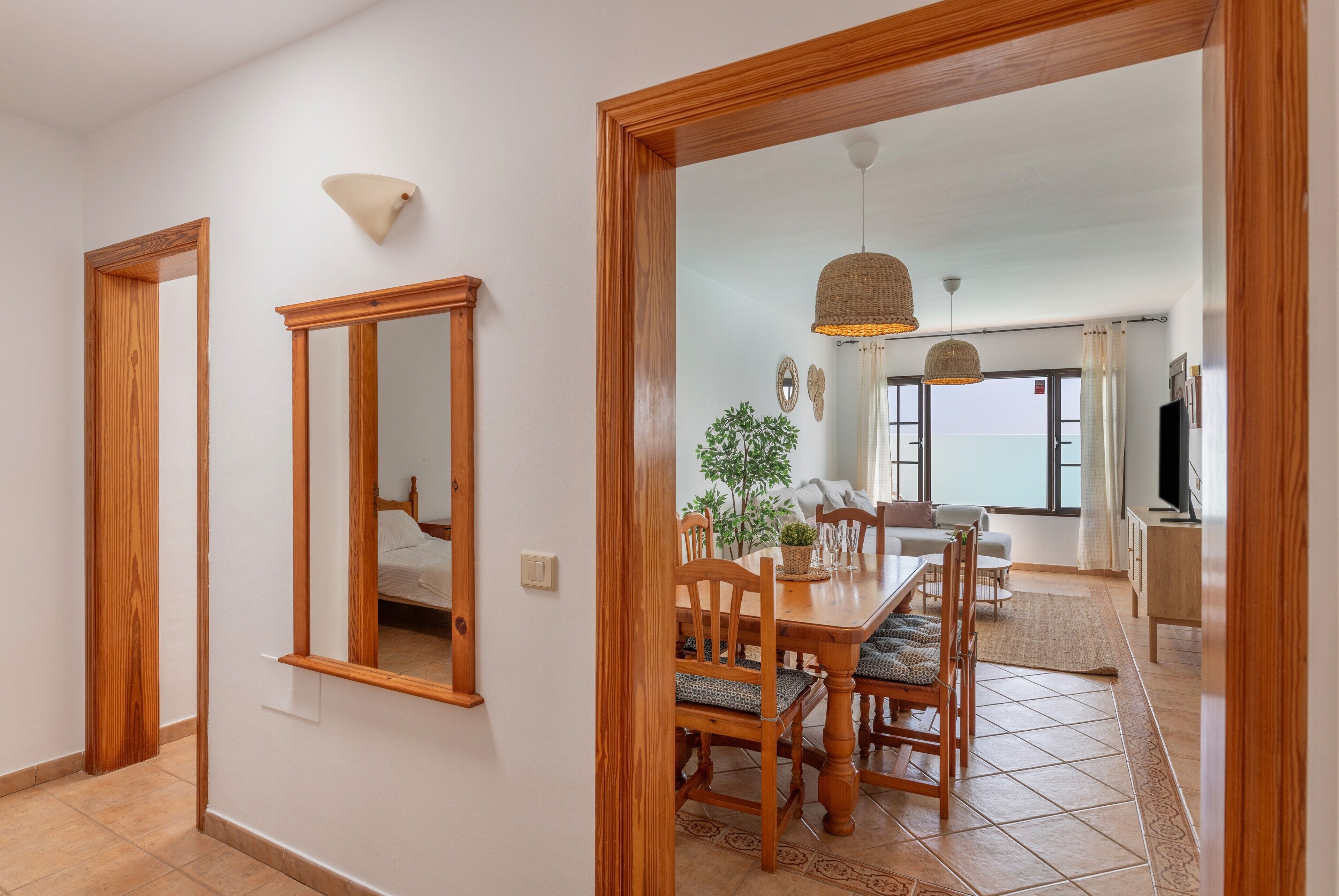 A dining area with a wooden table and chairs, a mirror, and a view of the sea through large windows.